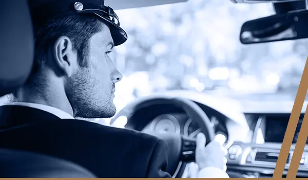 A man in a suit is driving a car, and he is looking towards the right-side mirror.